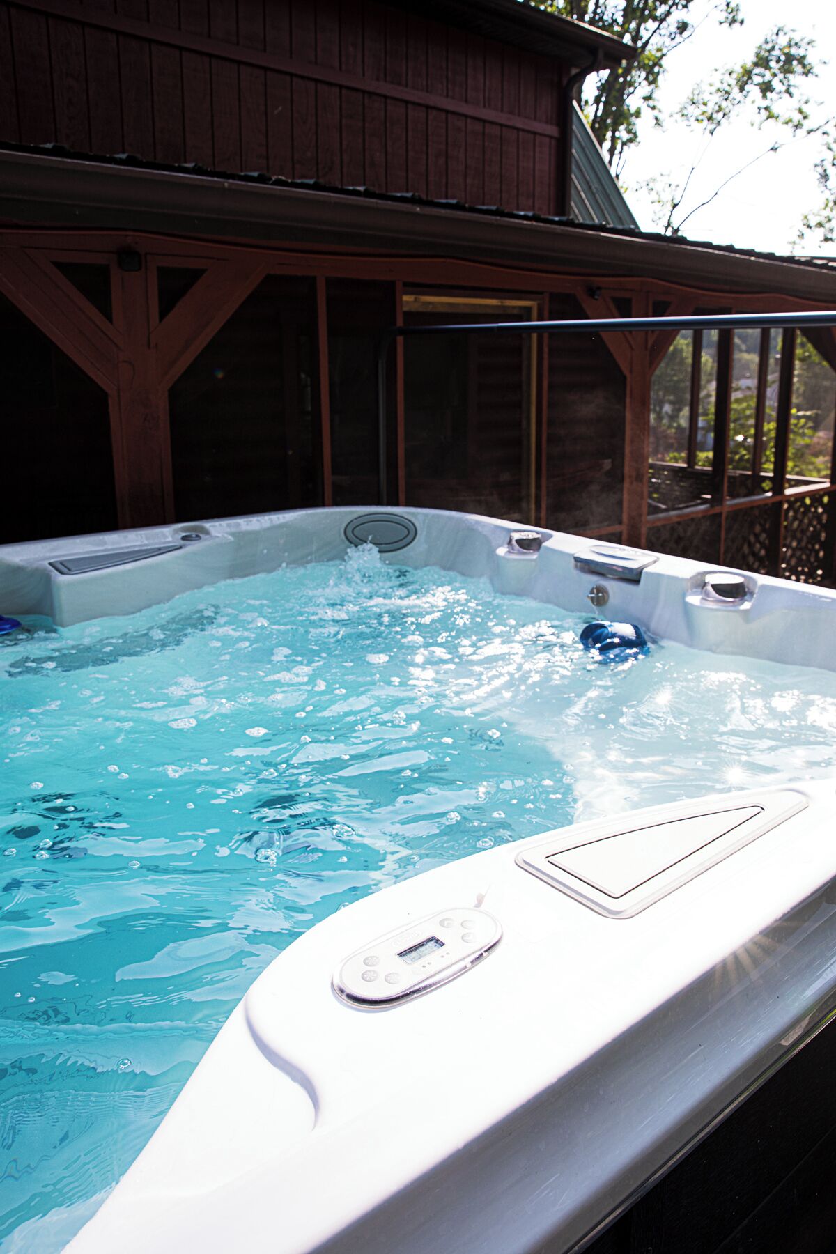 Un jacuzzi con panel de control, rodeado por una terraza de madera y un edificio al fondo.