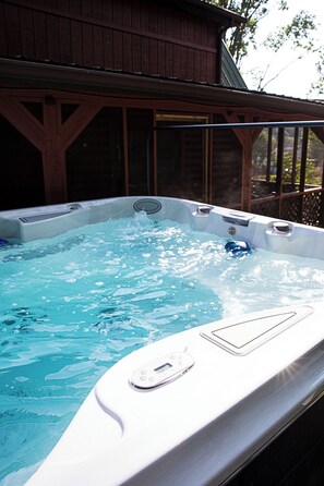 A hot tub with a control panel, surrounded by a wooden deck and a building in the background. - Cozy Cabin, Leaves 🍁 Private Swim Jacuzzi Spa- Beautiful Gardens & Orchard   (Jonesborough)