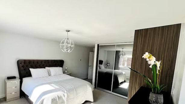 A modern bedroom with a large bed, a nightstand, a mirror, and a potted orchid. - Horley Hideaway - 4 Bedroom House- Sleeps 7 (Horley)