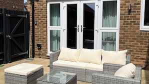 A wicker sofa with cushions, a glass-top coffee table, and a black gate in a brick building. - Horley Hideaway - 4 Bedroom House- Sleeps 7 (Horley)