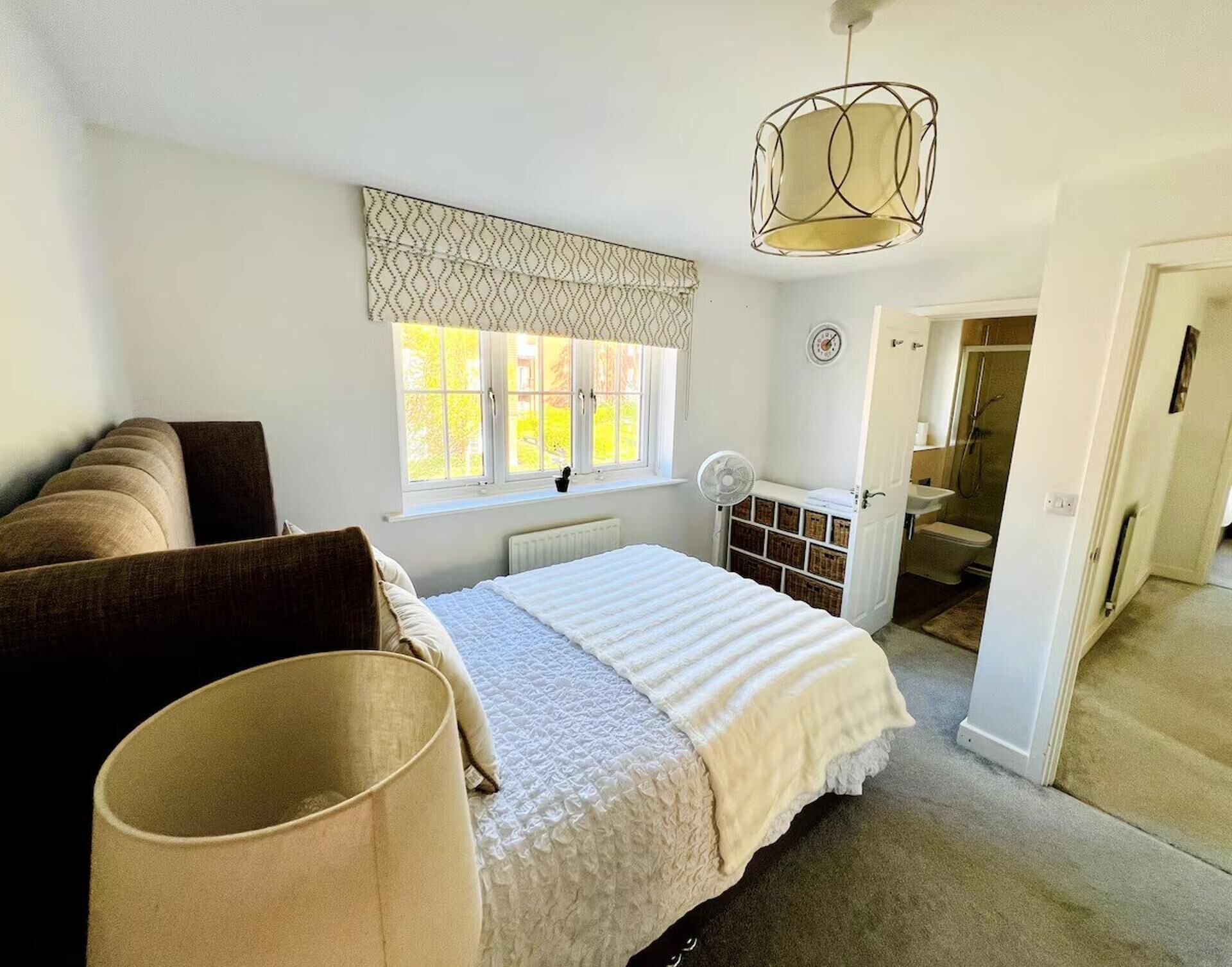 Um quarto com cama, luminária de cabeceira, janela com cortinas e porta para um banheiro.