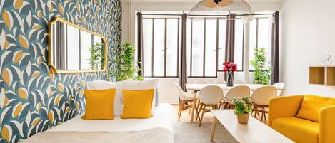 Una habitación de hotel moderna con una cama grande, un área de comedor con mesa y sillas, y un sofá.