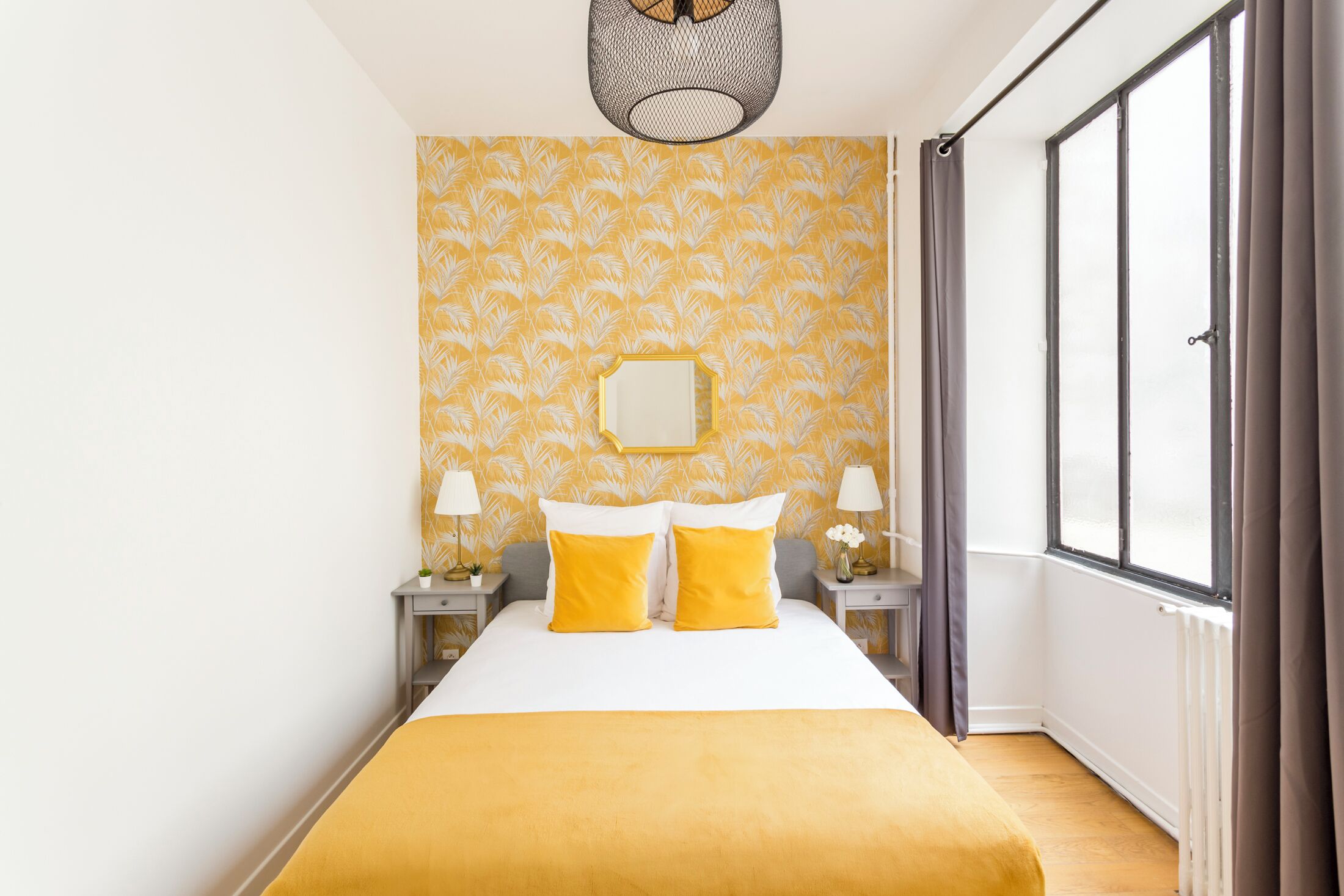 A hotel room with a large bed, two bedside tables with lamps, a mirror on the wall, and a window with curtains.