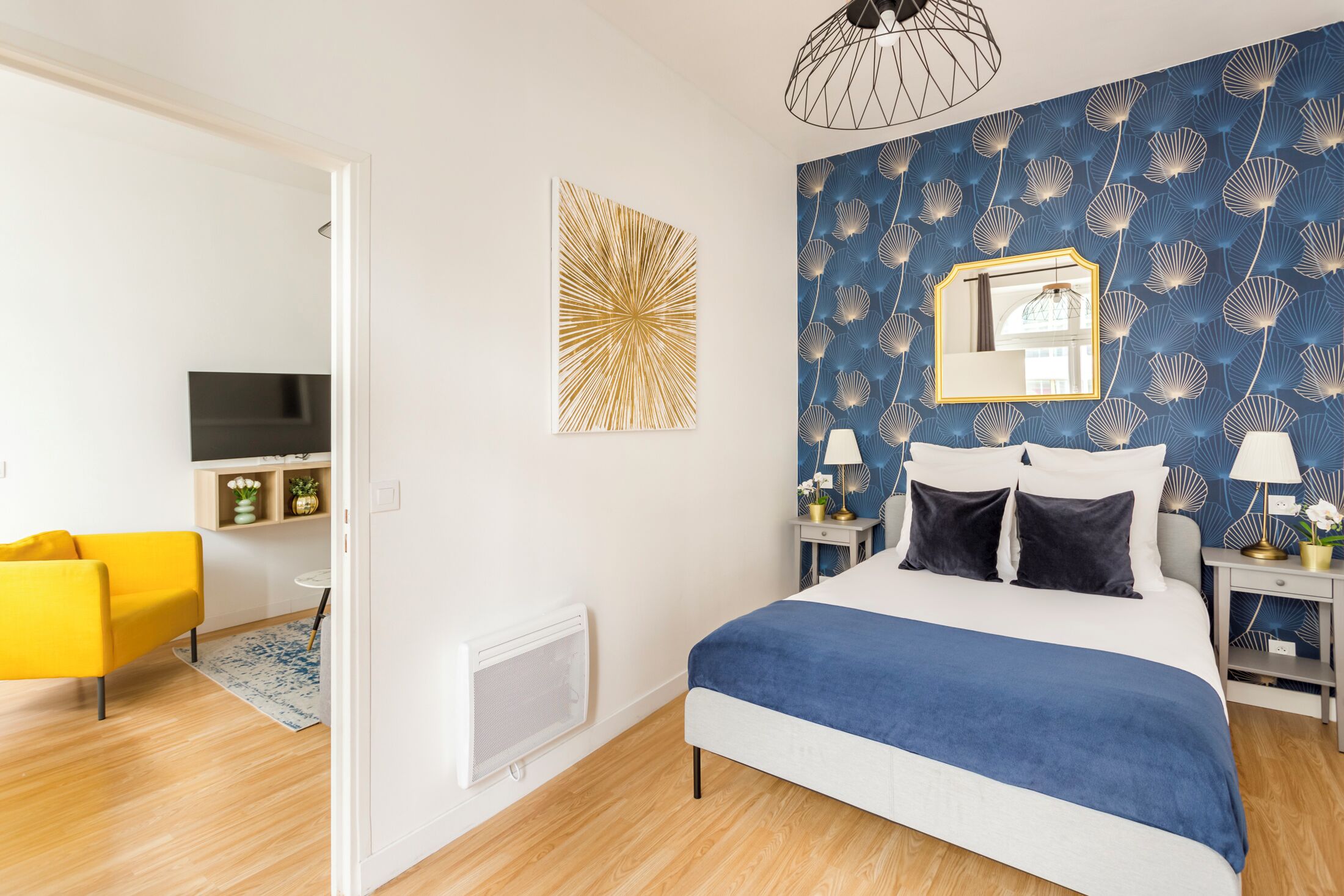 A bedroom with a bed, a yellow armchair, a TV, and a blue patterned wall.