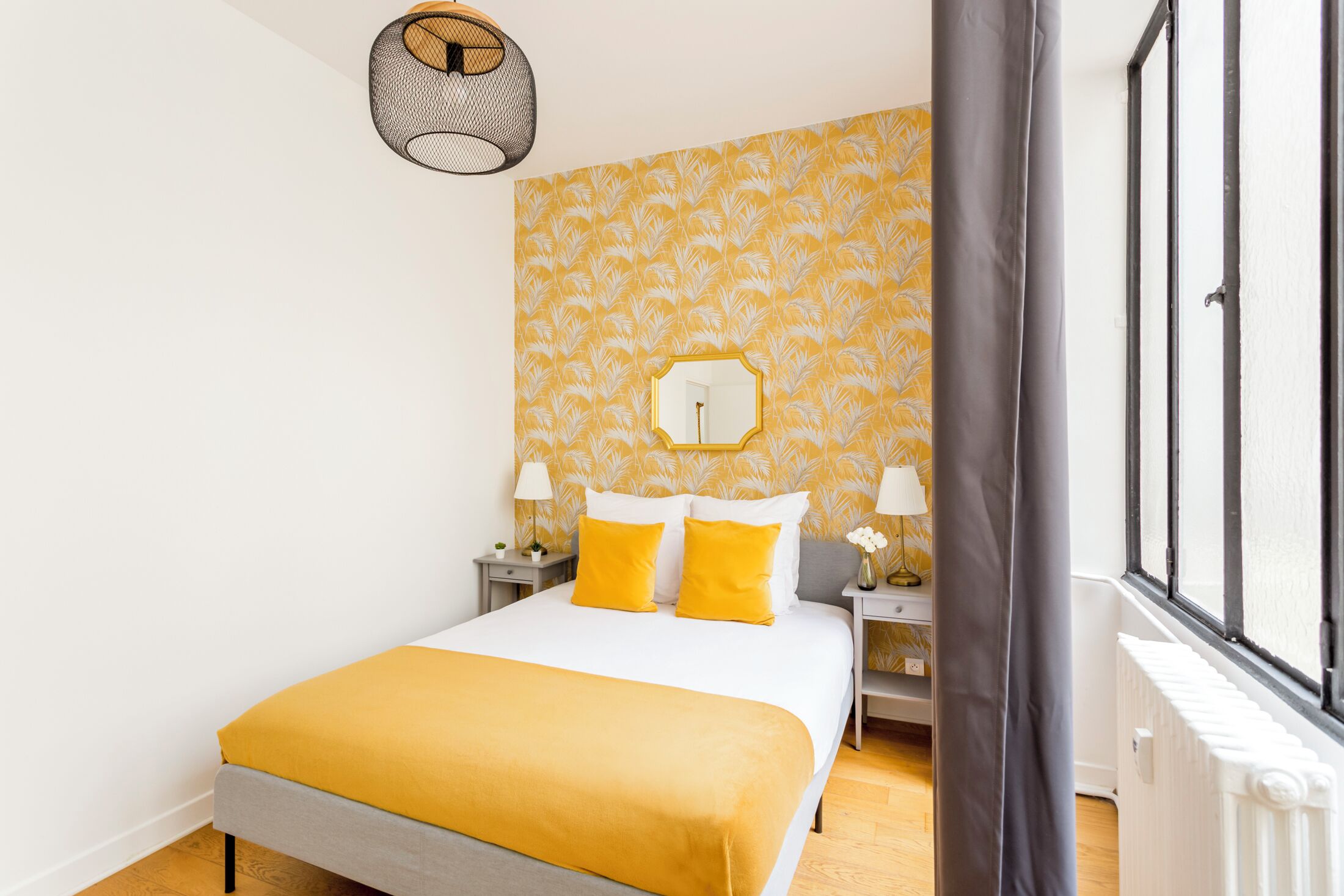 Een verzorgde slaapkamer met een bed, twee nachtkastjes, een spiegel en een raam met gordijnen.