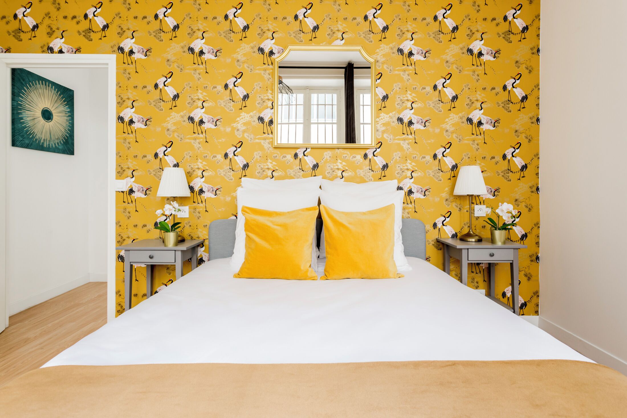Habitación de hotel con cama, dos mesitas de noche, un espejo y papel tapiz amarillo con motivos florales.
