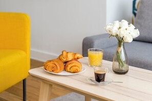 Une table en bois dressée pour le petit-déjeuner, avec des croissants, du jus d’orange et du café.