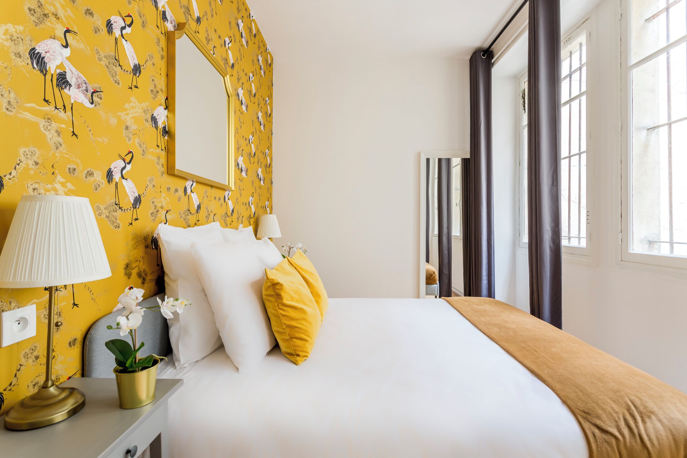 Una habitación de hotel con cama, mesita de noche, lámpara y espejo.