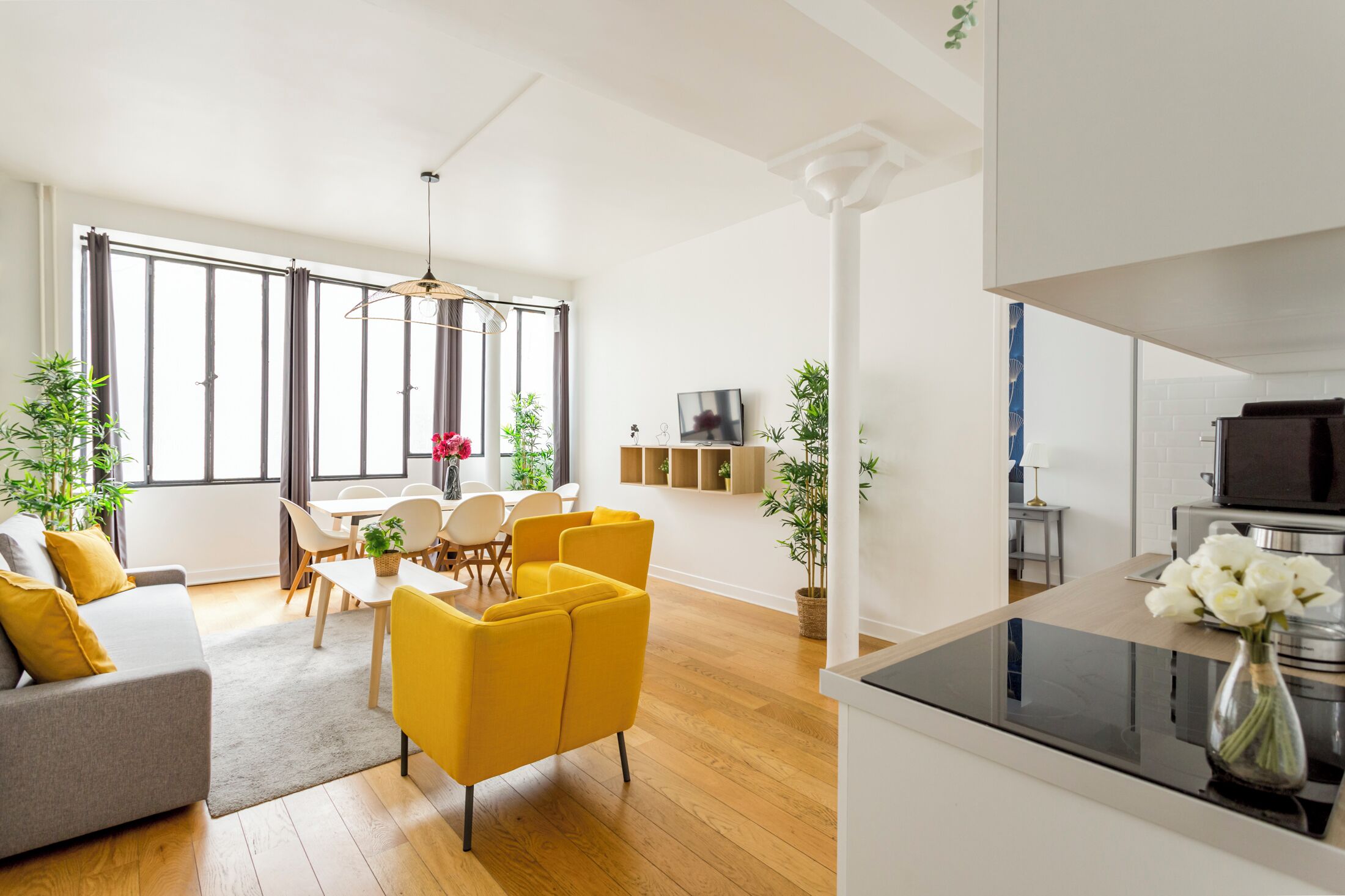 A modern living room with a sofa, yellow chairs, a dining table, and a kitchen area with a TV and stove.