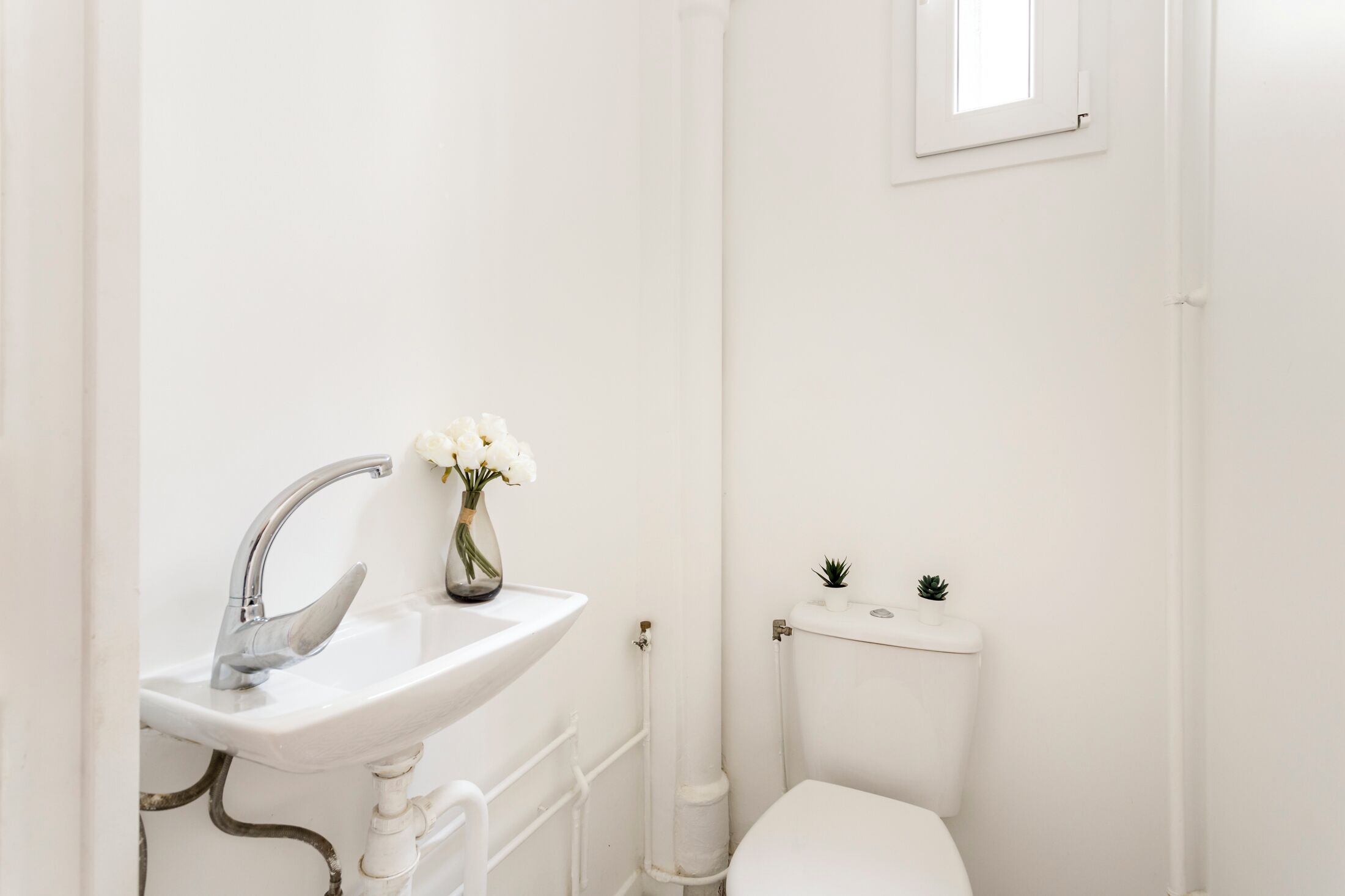 Un bagno bianco con lavandino, wc e una piccola finestra.