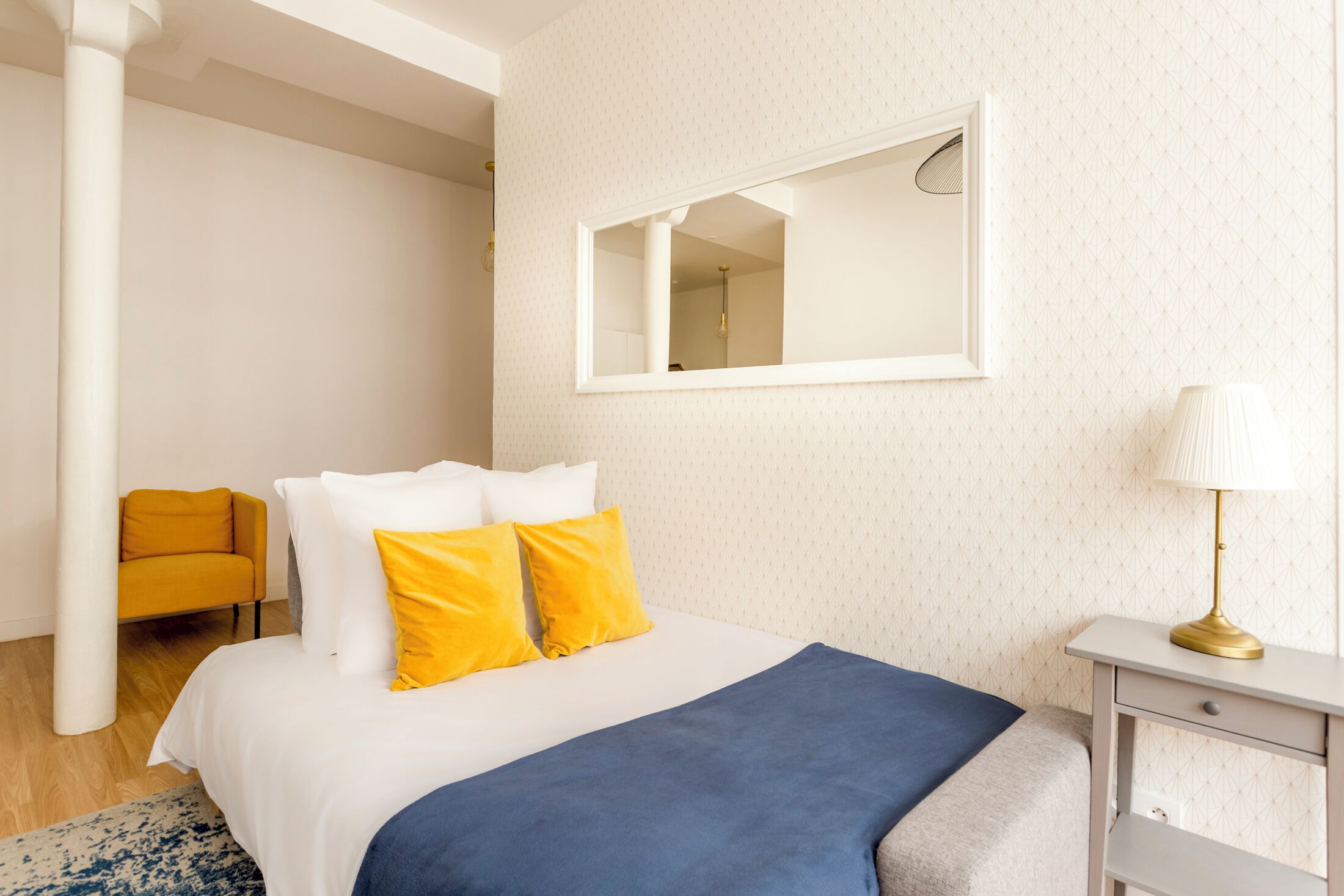 A bedroom with a bed, a mirror, a lamp, a chair, and a nightstand.