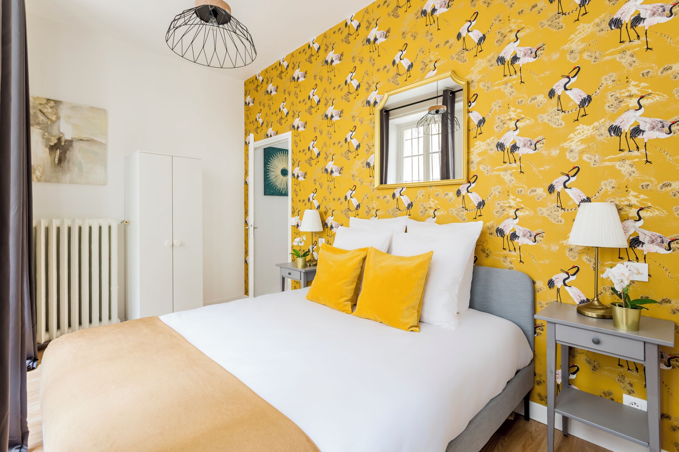 A hotel room with a bed, a nightstand, a lamp, a mirror, and a radiator.