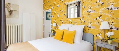 A hotel room with a bed, a nightstand, a lamp, a mirror, and a radiator.