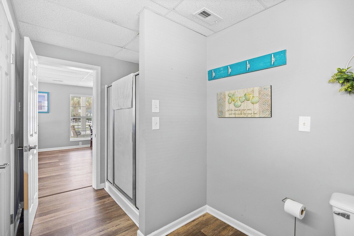 A hallway with a door leading to a bathroom, a wall-mounted towel rack, and a framed artwork.