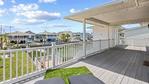 Une terrasse extérieure couverte avec une balustrade blanche, un petit espace gazonné et une vue sur une marina avec des bateaux.