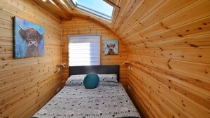 A cozy room with wooden walls, a skylight, a bed with patterned bedding, and two paintings on the walls.