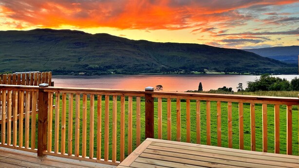A wooden deck with a view of a lake and hills during sunset.