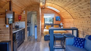 Ein gemütliches, kleines Blockhaus mit Küche, Essbereich und einem kleinen Wohnraum inklusive Sofa und Barhocker.