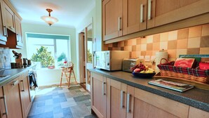 A modern kitchen with wooden cabinets, a microwave, toaster, and a bowl of fruit on the counter. - Bryn Tor (Bolsover)