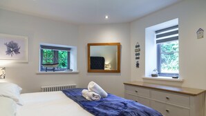 Un dormitorio con una cama, dos ventanas, un aparador y un espejo.