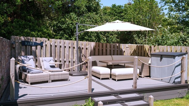 Una terraza con mobiliario de mimbre, una mesa y una sombrilla.