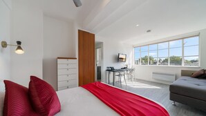A modern bedroom with a large bed, red pillows, a desk, and a grey sofa.