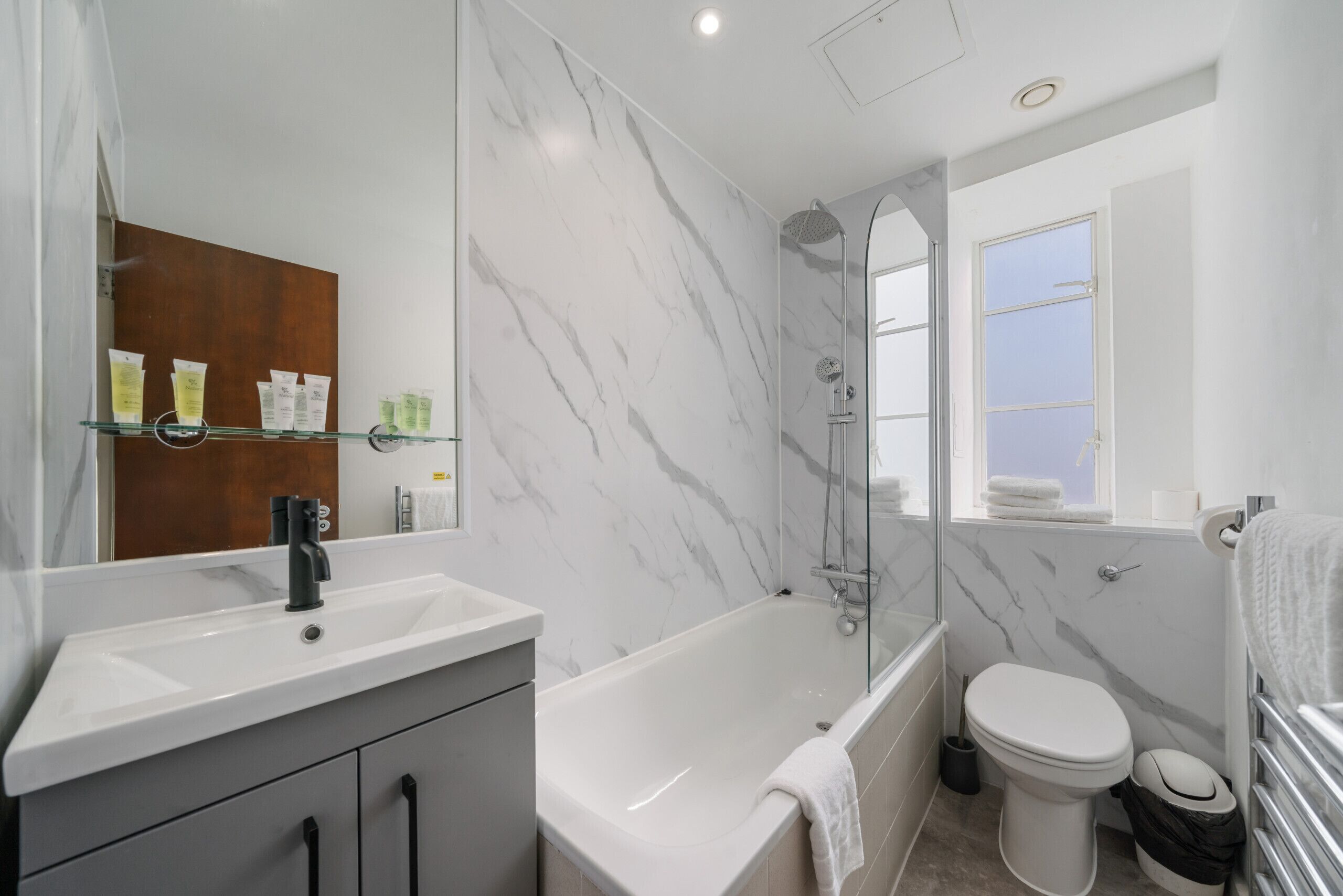 Ein modernes Badezimmer mit einem weißen Waschbecken, einer Badewanne, einer Toilette und einer gläsernen Dusche.