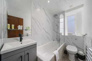 Une salle de bain moderne avec un lavabo blanc, une baignoire, des toilettes et une douche à parois de verre.