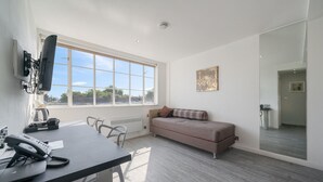 A modern room with a large window, a sofa, a desk with a telephone, and a mounted television.