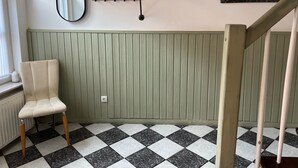 A room with a checkered floor, a radiator, a chair, a coat rack, a mirror, and a picture of a ship.