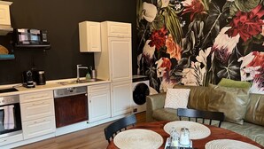 A modern kitchen with white cabinetry, a built-in oven, and a microwave. There is a dining table with placemats and a remote control.