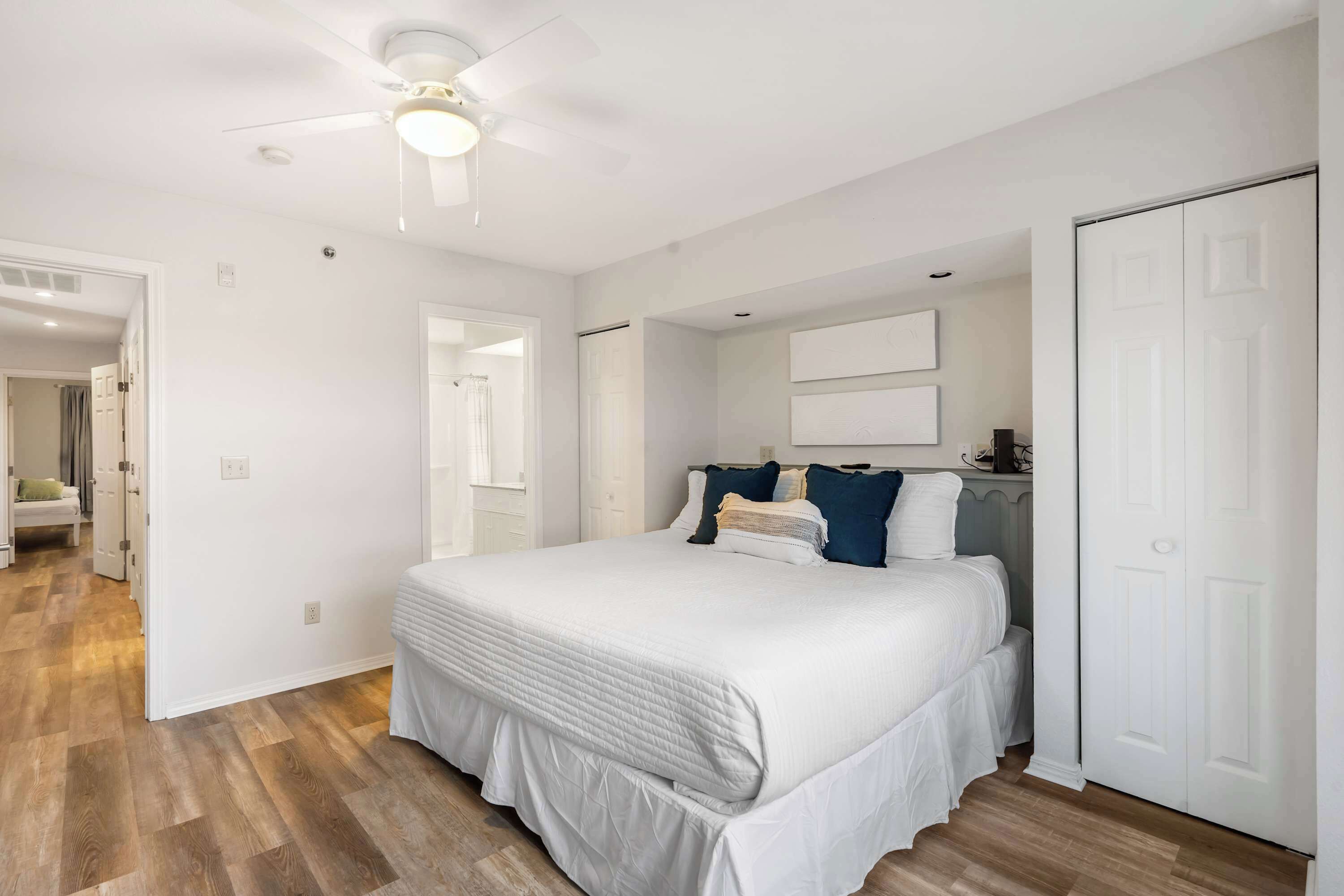 A bedroom with a large bed, a ceiling fan, and a white door.