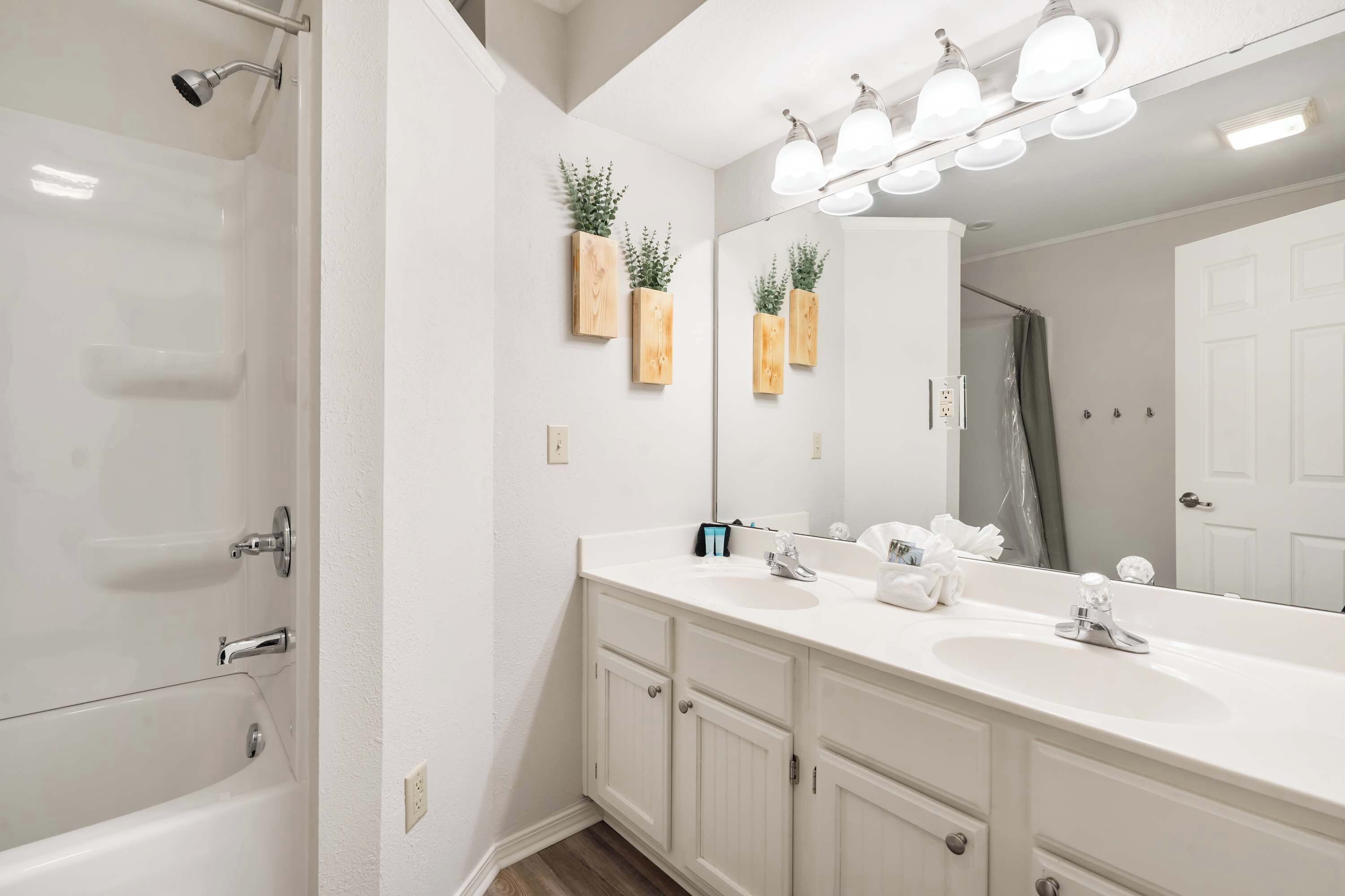 A modern bathroom with a white vanity, double sinks, a large mirror, and a shower.