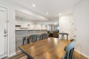 Een eetgedeelte met een houten tafel en stoelen, witte kasten en een keuken op de achtergrond.