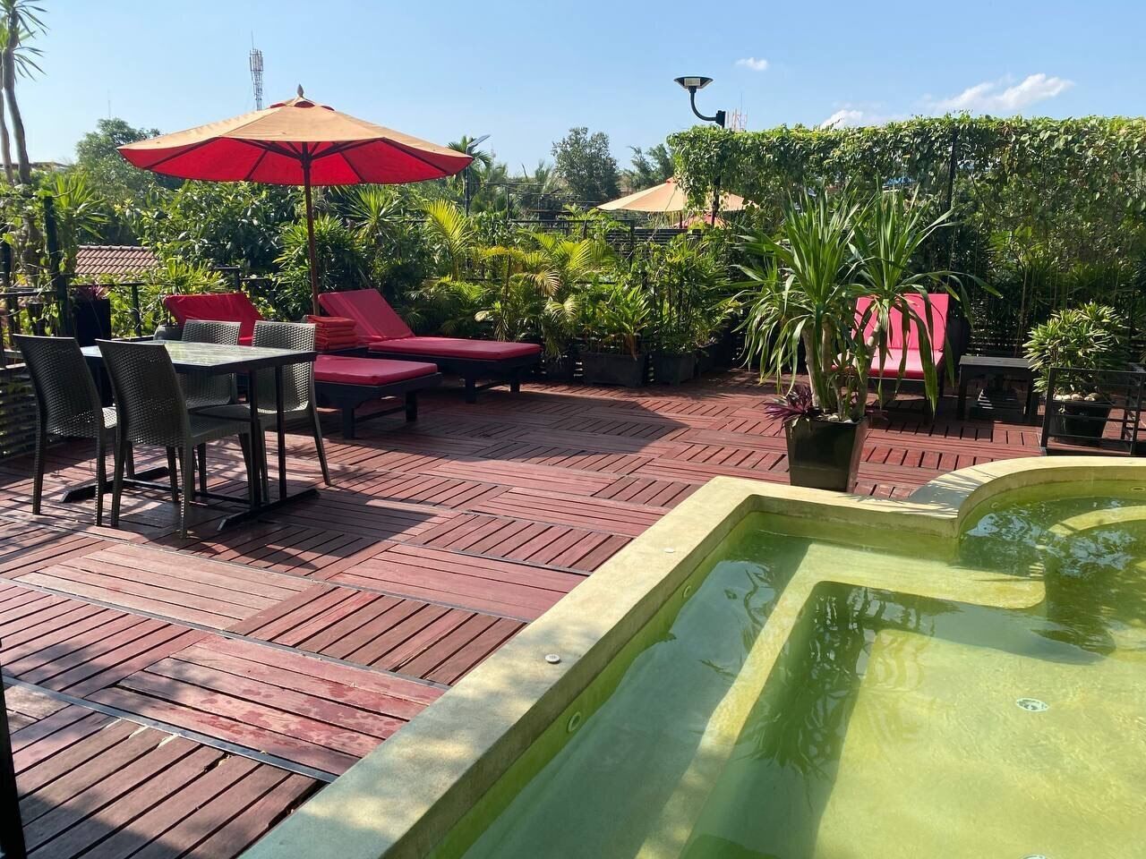 Une terrasse sur le toit avec un sol rouge, un jacuzzi et des sièges d’extérieur protégés par des parasols.
