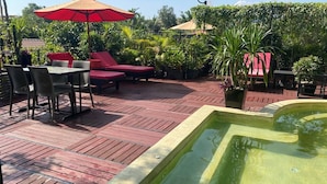 A rooftop patio with red flooring, a hot tub, and outdoor seating with umbrellas.