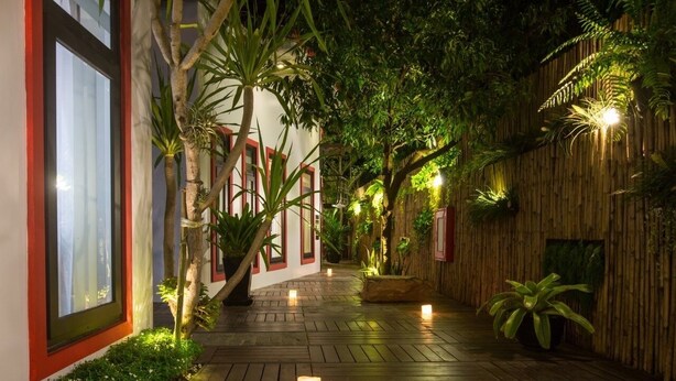 A wooden pathway with potted plants and candles, leading to a building with red-framed windows.