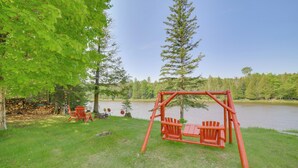 A wooden swing set with two chairs in a grassy area near a lake, surrounded by trees. - Escanaba River Getaway: Fish, Hike & Ski! (Cornell)