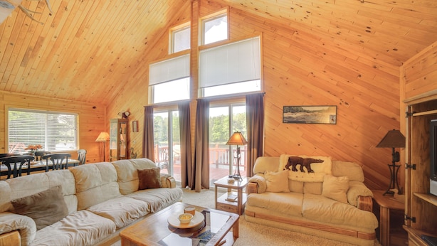 A spacious living room with high ceilings and large windows, furnished with sofas and a coffee table. - Escanaba River Getaway: Fish, Hike & Ski! (Cornell)