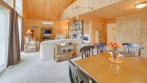 A cozy cabin interior with a wooden ceiling, a living area with a sofa and TV, a dining table with chairs, and a stone fireplace. - Escanaba River Getaway: Fish, Hike & Ski! (Cornell)
