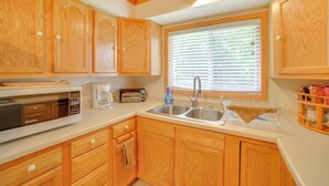 A kitchen with wooden cabinets, a microwave, a toaster, and a sink. - Escanaba River Getaway: Fish, Hike & Ski! (Cornell)