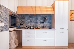 Una cucina compatta con mobili bianchi, forno integrato e parete rivestita di piastrelle.