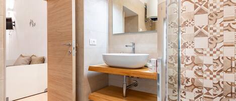 Un baño moderno con tocador de madera, un lavamanos blanco y una zona de ducha con diseño.