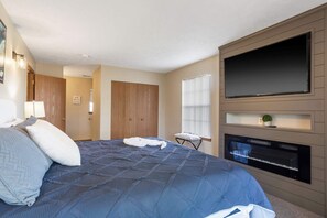 Un dormitorio con una cama grande, un televisor de pantalla plana en la pared, una mesita y una ventana con persianas.