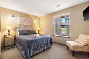 A neatly arranged bedroom with a large bed, bedside lamps, a chair, and a window with bars. - Pond View Serenity For 6! (Branson)