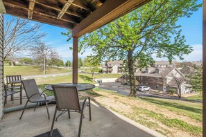 A covered patio with outdoor seating, overlooking a residential area with houses and a tree. - Pond View Serenity For 6! (Branson)