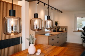 A modern kitchen with pendant lights, a wooden dining table, and a vase with a plant. - Apartment 'Fewo Tauberblick' with Shared Terrace, Private Garden and Wi-Fi (Röttingen)