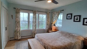 Ein Schlafzimmer mit Bett, Nachttisch, Lampe und einem Fenster mit Vorhängen.