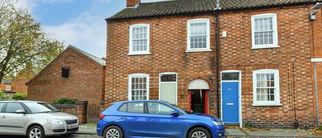 A two-story brick house with a red door and a blue door, two windows, and a chimney.
