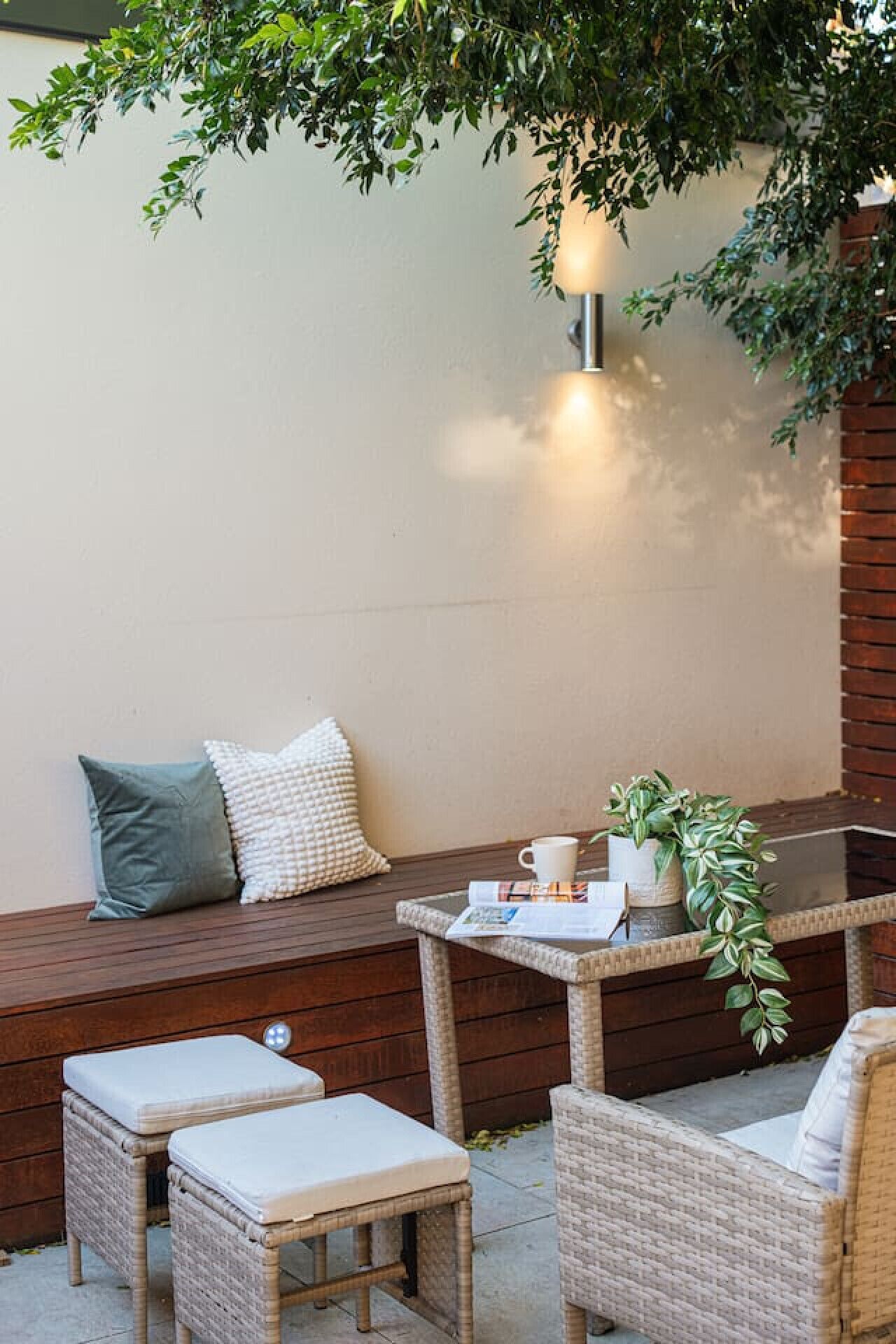 A cozy outdoor seating area with wicker furniture, a table with a cup and a plant, and a wall-mounted light fixture.